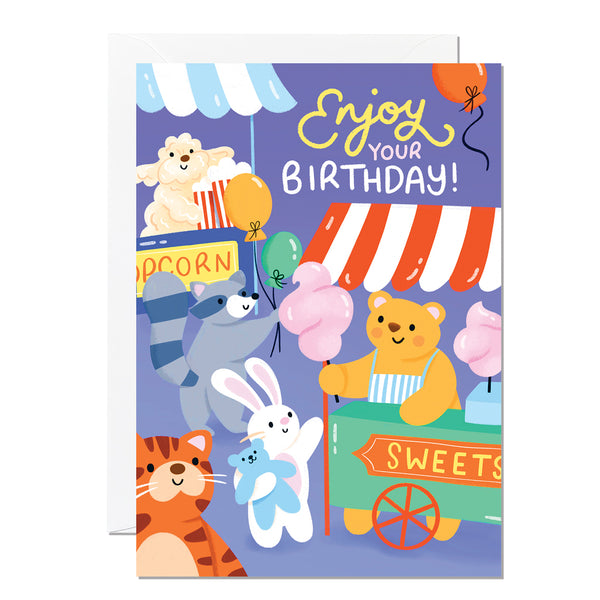 A colourful birthday card featuring cartoon animals at a carnival with balloons and a banner saying 'Enjoy your Birthday!'