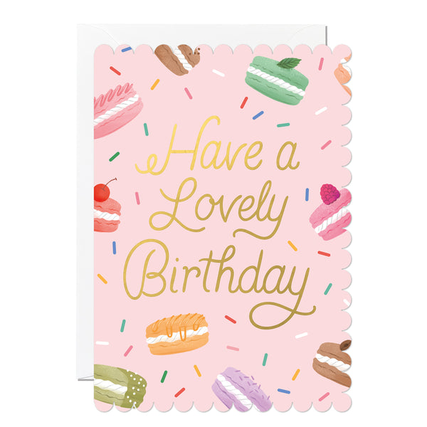 Birthday card with 'Have a Lovely Birthday' text, illustrations of macarons and colourful sprinkles on a pink background