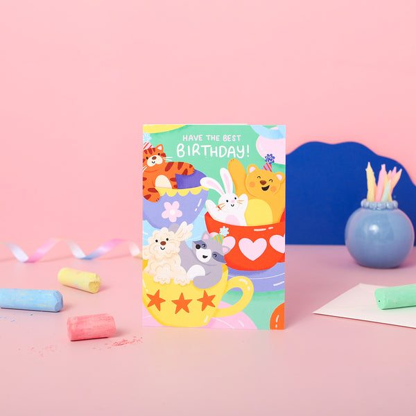 A colourful birthday card featuring cartoon animals having fun on the teacups ride at the funfair, with a 'Happy Birthday' message.