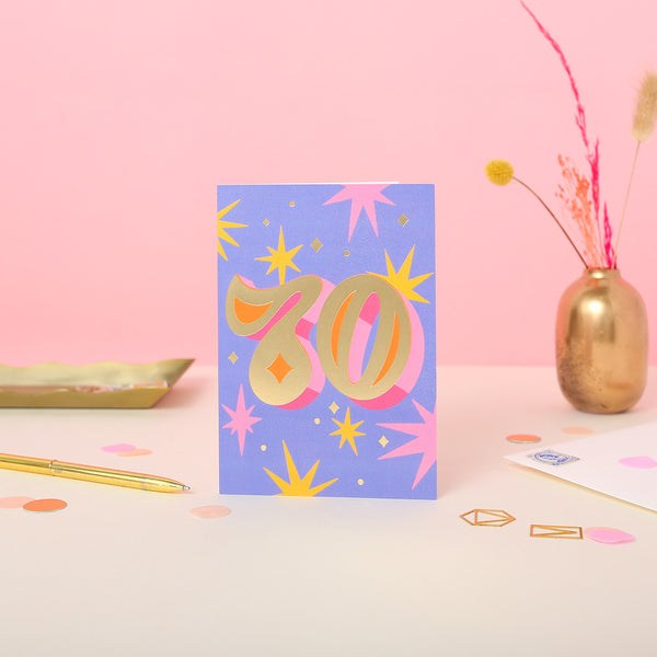 A 70th birthday card with a purple background and star illustrations with a white envelope.