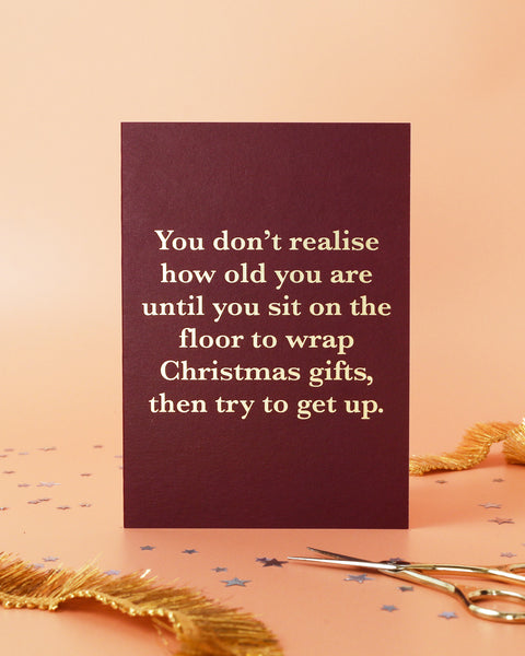 Maroon card with humorous text on a pink background with gold decorative elements.
