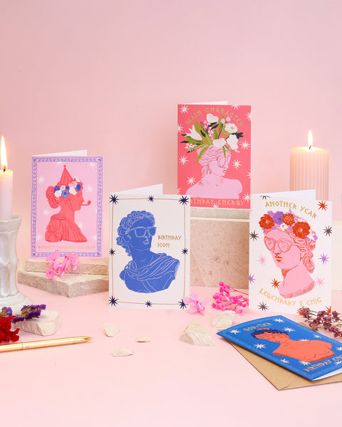 Collection of greeting cards on a pink surface with candles and decorative items.