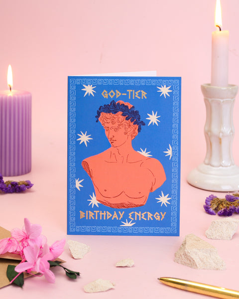 A classical-style birthday card showcasing a coral-toned Greek marble bust with a laurel wreath, set against a deep blue background with an ornate key border.
