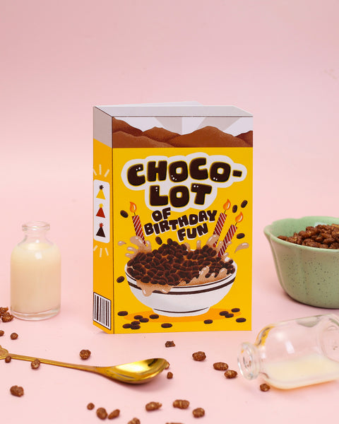 A die-cut greeting card designed as a chocolate cereal box, featuring a hand-illustrated splashing bowl of cocoa cereal and striped birthday candles.