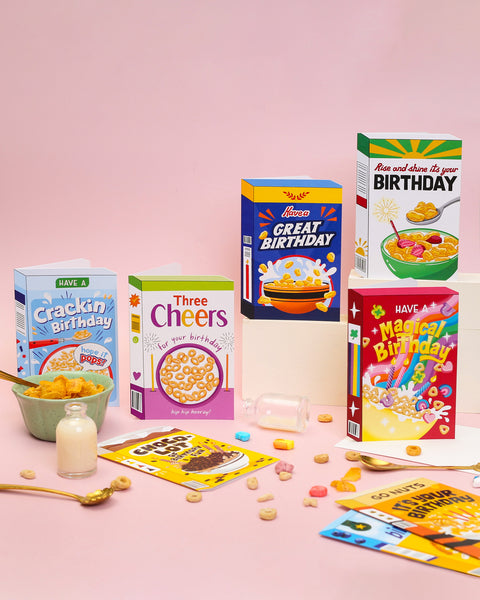 Collection of colourful birthday-themed cereal birthday cards and packaging on a pink background