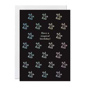A black birthday card featuring a pattern of magician's hats with a caption that reads 'have a magical birthday' printed with an iridescent foil