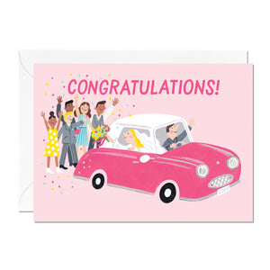 A wedding card that features a pink Nissan Figaro with a happy couple being congratulated by onlookers printed on a pink background