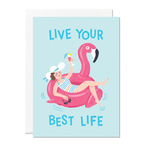 A birthday card that features an illustration of a woman holding a cocktail lounging on a flamingo pool float with a greeting that reads 'Live Your Best Life'