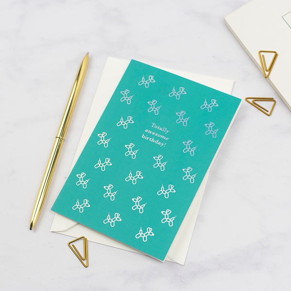 A totally awesome birthday card featuring a pattern of dog balloons on a green background printed with an iridescent foil