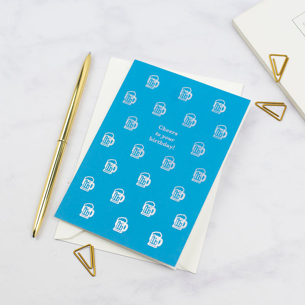 A blue birthday card with small graphic illustrations of a pint of beer printed with an iridescent foil