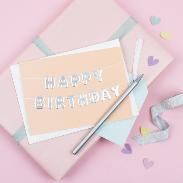 An orange birthday card with birthday bunting that reads 'happy birthday' printed with an embossed silver foil